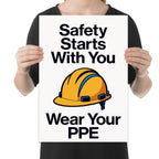 Safety Starts With You Wear Your PPE poster with bold black lettering and a yellow hard-hat illustration, shown held for scale